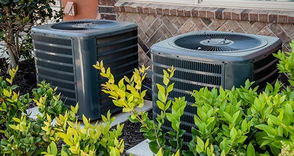 Two exterior A/c units outside with bushes surrounding them.