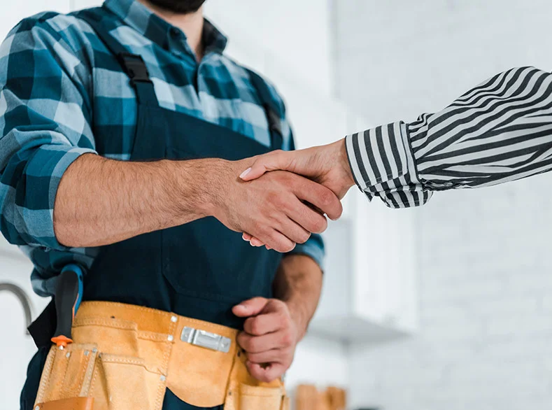 Two people shaking hands, one is wearing a tool belt and apron.